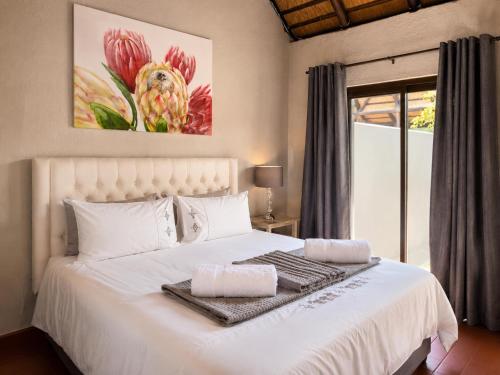 a bedroom with a white bed with a painting on the wall at Singwe Private Safari Lodge Kruger in Marloth Park