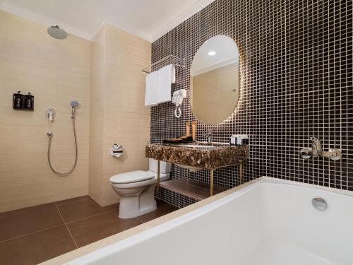 a bathroom with a tub and a toilet and a mirror at Elais by ARTOTEL in Medan