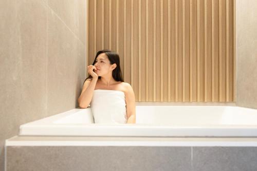 a woman sitting in a bath tub talking on a cell phone at Hotel Rivmont Danyang by Anook in Danyang
