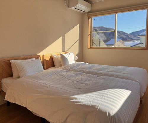 a large white bed in a bedroom with a window at Yamamori House in Hakuba