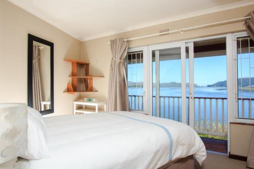 a bedroom with a white bed and large windows at Ilse's Garden Route Gem in Knysna