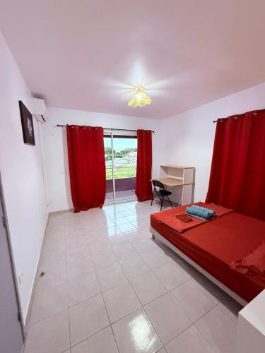 a bedroom with a bed and a desk and red curtains at Le Petit Refuge in Cayenne