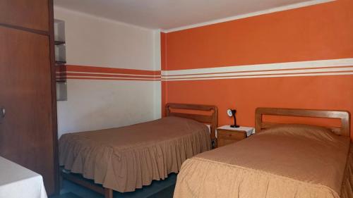 two beds in a room with orange walls at Hostal Churuquella in Sucre