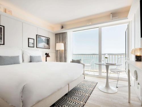 a white bedroom with a large bed and a table at Bel Hôtel Oléron Thalasso & Spa - MGallery Collection in Saint-Trojan-les-Bains