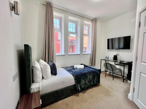 a bedroom with a bed and a desk and windows at The Anfield Hotel in Liverpool