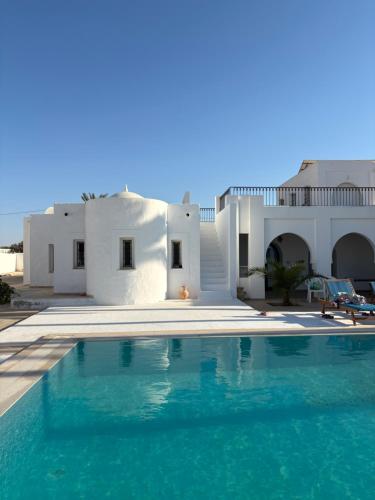 a swimming pool in front of a white house at Maison Rachid Djerba in El Guecheïne