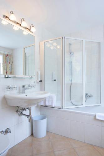 a white bathroom with a shower and a sink at Hotel Silbertal in Silbertal