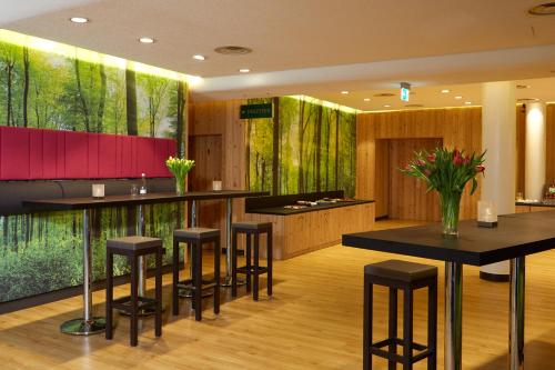 a bar with stools in a room with trees at Mercure Hotel am Messeplatz Offenburg in Offenburg