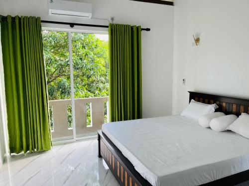 a bedroom with a bed with green curtains and a window at Letharo Residancies in Dodanduwa