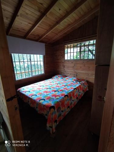 a bed in a wooden room with two windows at La Cabaña de Chia in Guarne