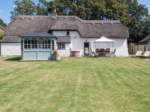 a white cottage with a thatched roof and a yard at Four Oaks in Bransgore