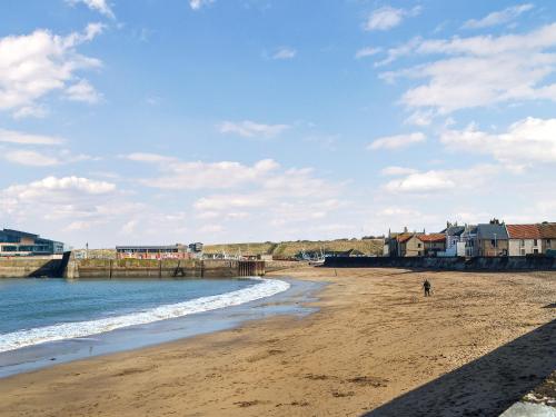 a person walking on a beach near the water at Doodles Holiday Home in Eyemouth