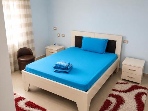 a bedroom with a bed with blue sheets and a chair at Shtepia e Bardhe in Patos