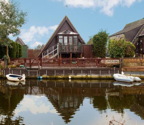 a house with two boats in the water at Isleham River Lodge in Isleham