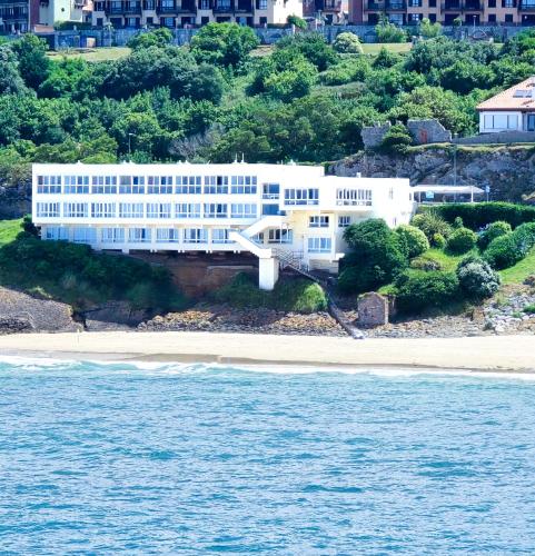 a white building on a beach next to the water at Hotel Josein in Comillas