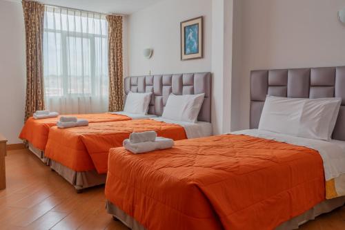 two beds in a hotel room with orange sheets at Hotel Libertad Pacasmayo in Pacasmayo