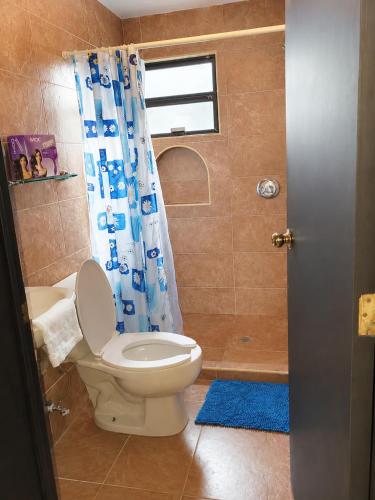 a bathroom with a toilet and a blue shower curtain at Villa Bonita Torre 16 in Cozumel