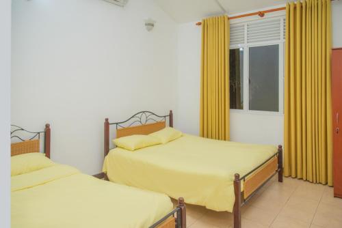 two beds in a room with yellow curtains and a window at Mango Villa in Kengalla