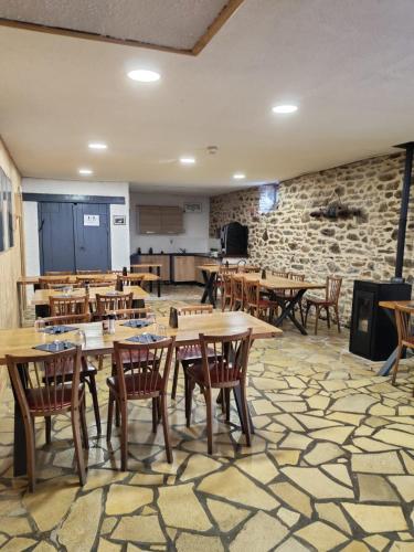 a restaurant with wooden tables and chairs and a stone wall at L'Embaradere in Laruns