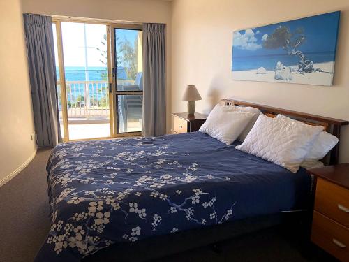 a bedroom with a bed with a blue blanket and a window at Sea Eagles Unit 4 in Caloundra