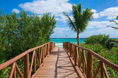 a wooden bridge leading to the beach with a palm tree at Unico Hotel Riviera Maya Adults Only in Akumal