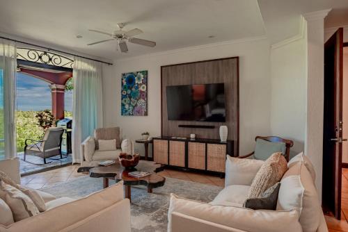 a living room with white furniture and a tv at Spacious 4BR Condo with Partial Ocean View - Bougainvillea - Reserva Conchal in Playa Conchal