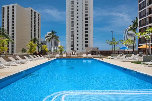 a swimming pool with lounge chairs and buildings at Waikiki Banyan 15FL - views, pool & hot tub access in Honolulu