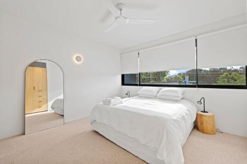 a white bedroom with a bed and a large window at Betula in Tilba Tilba
