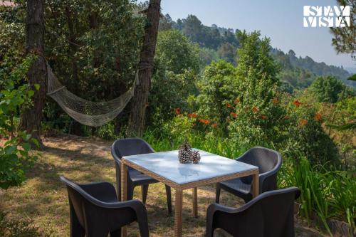 a table and chairs with a view of a forest at StayVista at Sukoon Nature Retreat in Bhatrojkhan