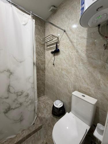 a bathroom with a white toilet and a shower at Квартира студия in Bosteri