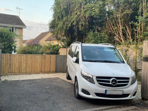 a white car parked in a driveway next to a fence at Cotswolds Vista Cirencester - Relaxed 5 Guest Home - 2 Bathroom, Parking, Garden in Cirencester