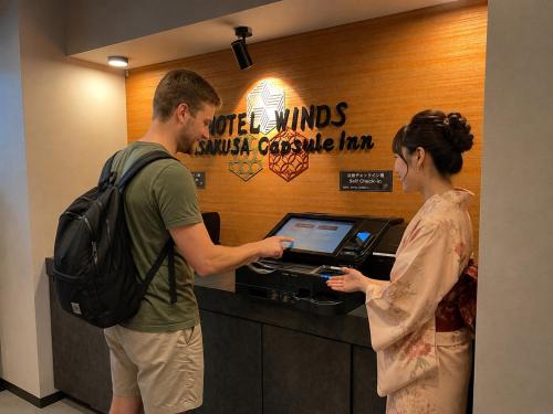 a man and a woman standing at a cash register at HOTEL WINDS ASAKUSA Capsule Inn 浅草 in Tokyo