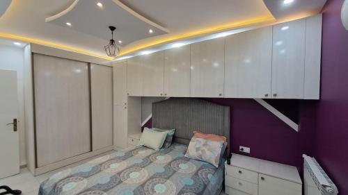 a bedroom with a bed with purple walls and white cabinets at Apartment rental for vacations in Boumerdes