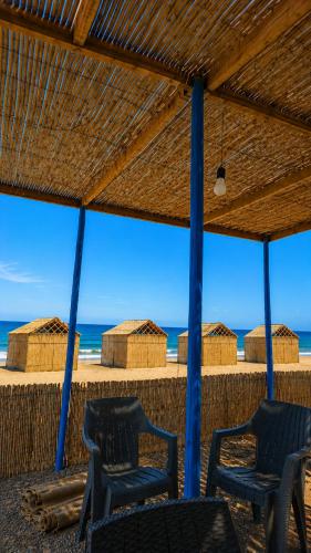 two chairs under a straw umbrella on the beach at ESPACE AZAiMi in Tarîfa