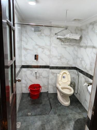 a bathroom with a toilet and a red bucket at The Green Shadow Business Hotel in Chittagong