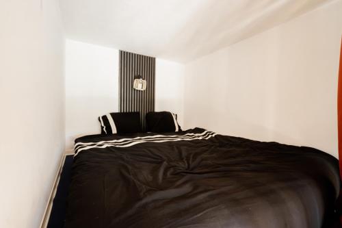 a bedroom with a black bed in a white room at Le Nid Cozy - Appart avec Piscine, Terrain de Tenis et Balcon in Métabief