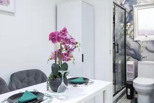 a table with purple flowers in a room with a toilet at Studio - Sleeps 2 - 5 Min to Trains - Parking in Thornton Heath