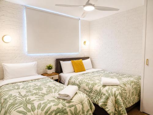 two beds in a small room with white walls at Dunes Apartment Unit 8- GROUND FLOOR WITH POOL VIEW in Coffs Harbour