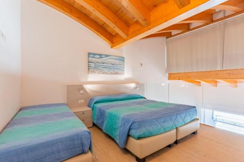 two beds in a room with white walls and wooden ceilings at Residenza Turistica Alberghiera Blue Marine in Bibione
