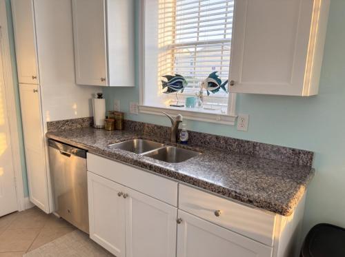 a kitchen with white cabinets and a sink and a window at Modern condo right across from beach and pool in Galveston