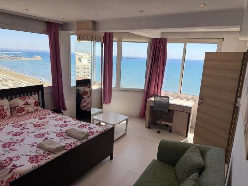 a bedroom with a bed and a desk and windows at Larnaca Seaview Rooms in Larnaca