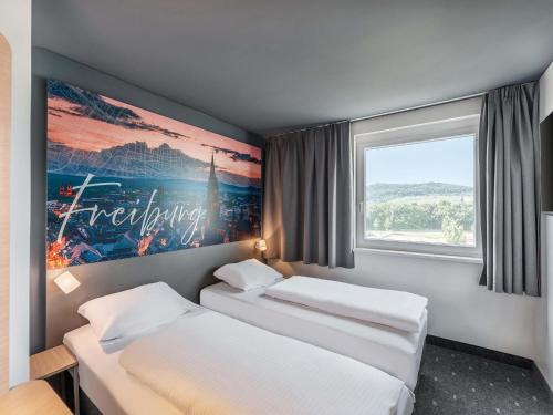 two beds in a hotel room with a large window at B&B Hotel Freiburg-Süd in Freiburg im Breisgau