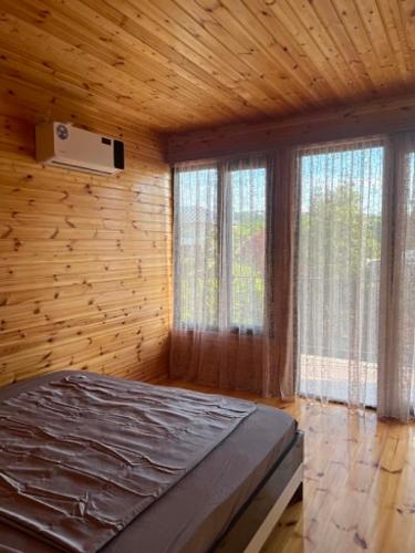 a bedroom with a bed in a wooden room with windows at Cottage Sandro-Sandrooo in Khuts'ubani