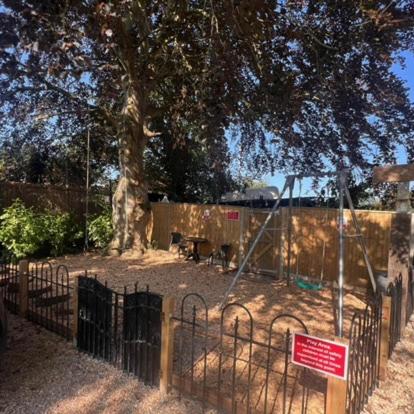 a playground with a tree and a fence with a sign at Hunston Mill Self Catering Dog Stay For Free in Chichester