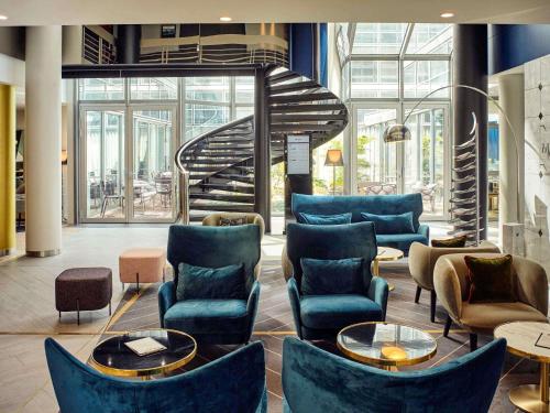 a lobby with blue chairs and a spiral staircase at Mercure Paris la Défense Grande Arche in Nanterre