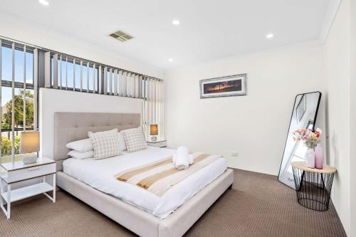a white bedroom with a large bed and a window at 4 bedroom luxury modern home near the beach and parks in Alkimos