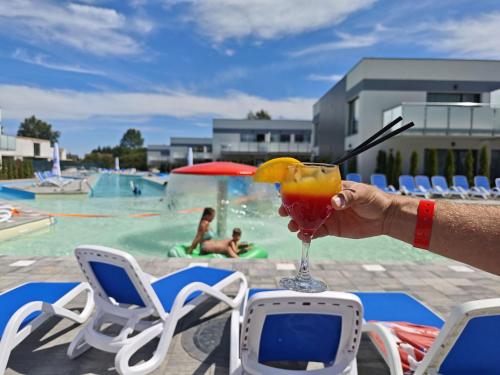a person holding a drink in front of a pool at Hotel i Apartamenty Gorzelanny Dźwirzyno in Dźwirzyno