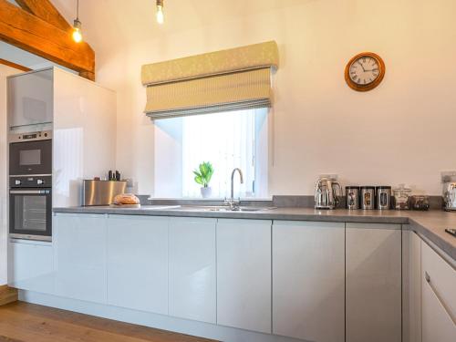 a kitchen with white cabinets and a clock on the wall at The Cottage - Ukc9711 in Winster