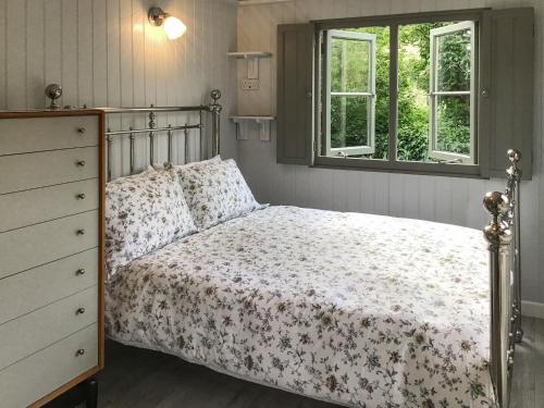 a bedroom with a bed and a dresser and two windows at Fig Tree Shepherds Hut in Bridport