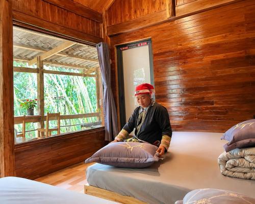a man sitting on a bed in a room with pillows at Red Dao Homestay and Entire bungalow in Tả Van